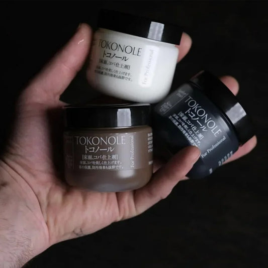 Tokonole burnishing gum jars in clear, brown, and black colors held in a hand.