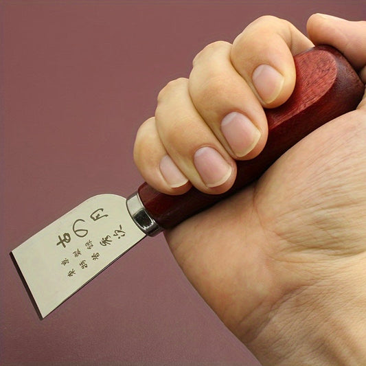 Leather cutting knife held in hand with dark red wooden handle and steel blade