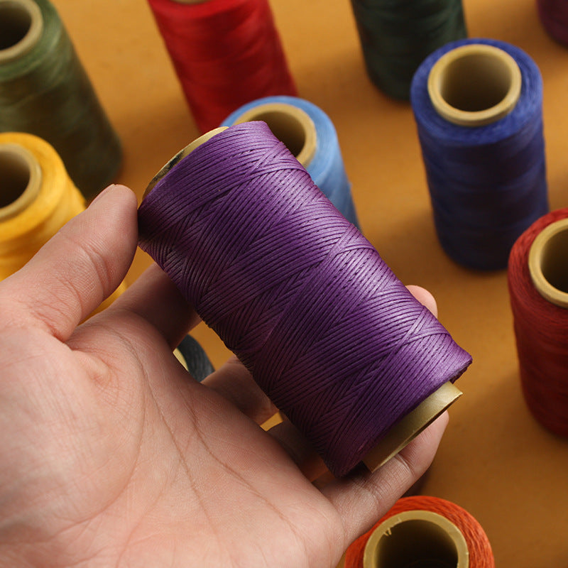 Purple waxed polyester stitching thread spool, held in hand for leather sewing