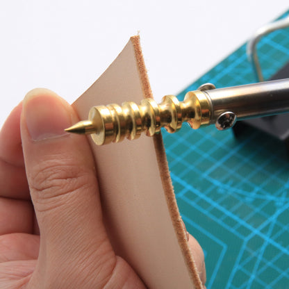 Gold-colored tool being used on a piece of leather with a blue cutting mat in the background