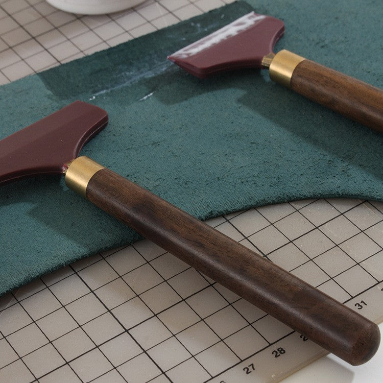 Silicone glue scraper spreader tool with maroon rubber head, dark wood handle, brass collar