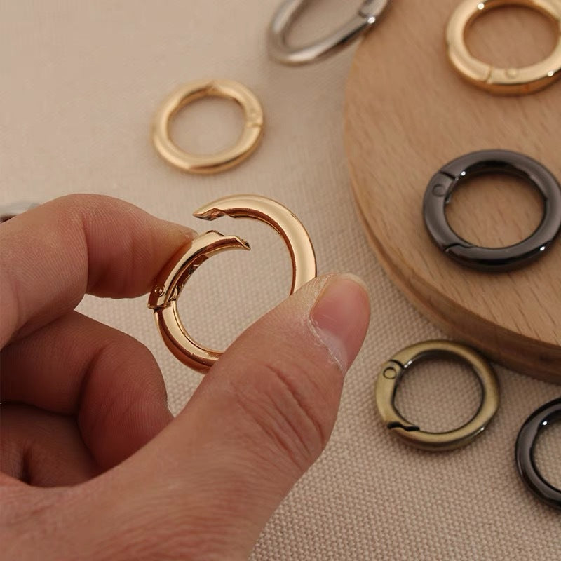 Gold-finish zinc alloy spring open split ring held by hand; other rings nearby