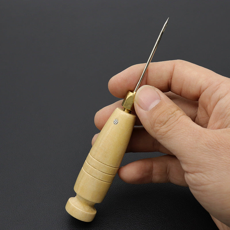Wooden sewing awl with brass head held in hand, featuring a metal needle tip