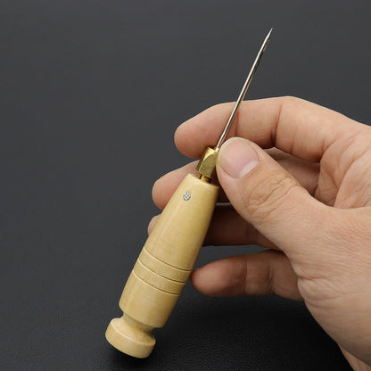 Wooden sewing awl with brass head held in hand, featuring a metal needle tip