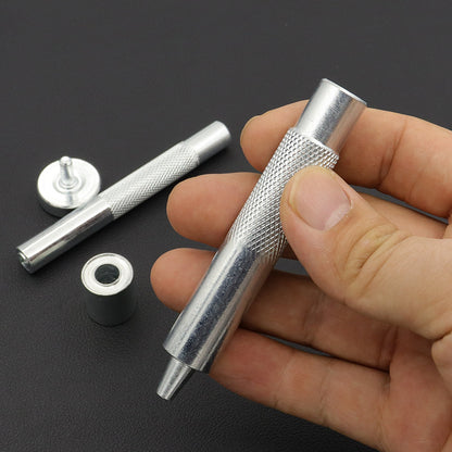 Handheld grommet setter tool with base die and metal eyelet rings, close-up