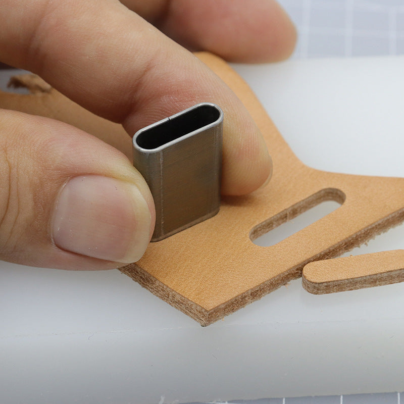 Hand holding an oblong slot punch die over leather strap with matching cut opening
