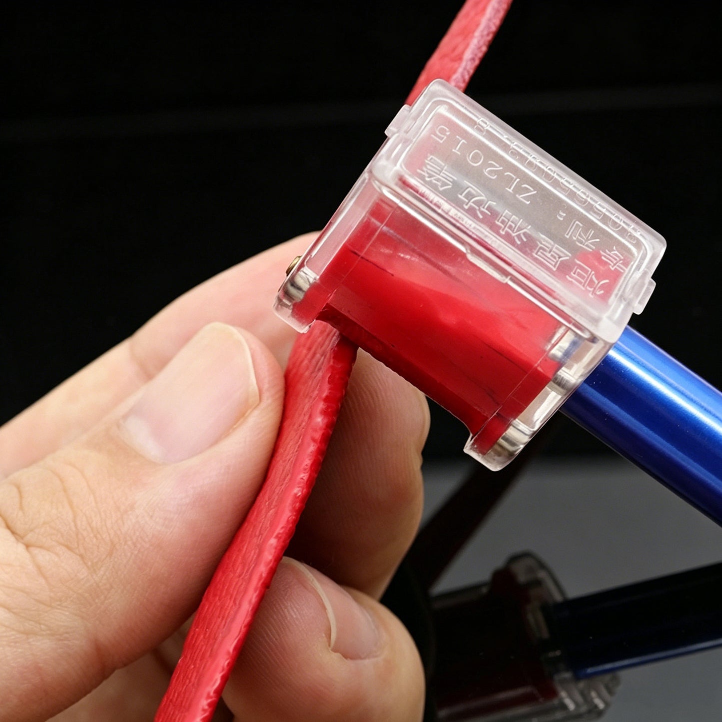 Red leather edge oil applicator pen with transparent roller head and gold roller tip, held in hand