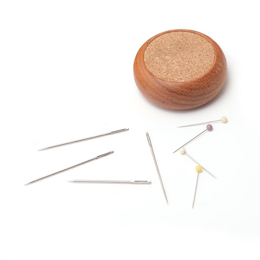 Brown round cork needle holder with several sewing needles and bead-topped tips